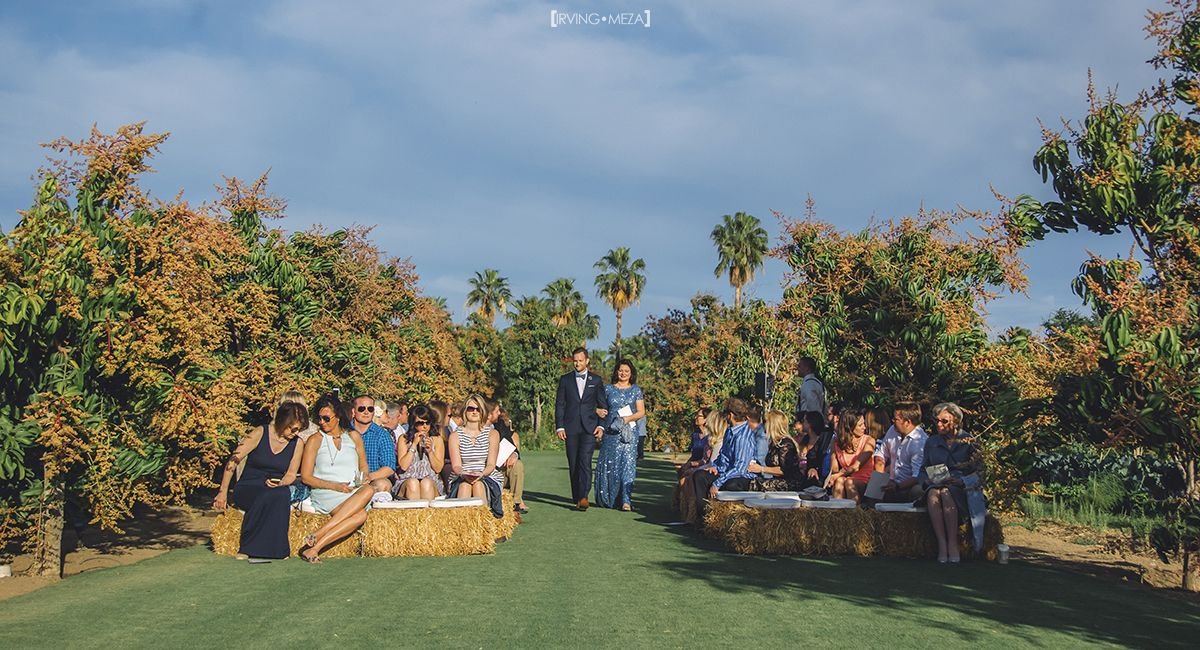 Wedding Ceremony at Wedding Venue Flora Farms in Cabo San Lucas, Mexico. The Groom is walking down the aisle with his mother