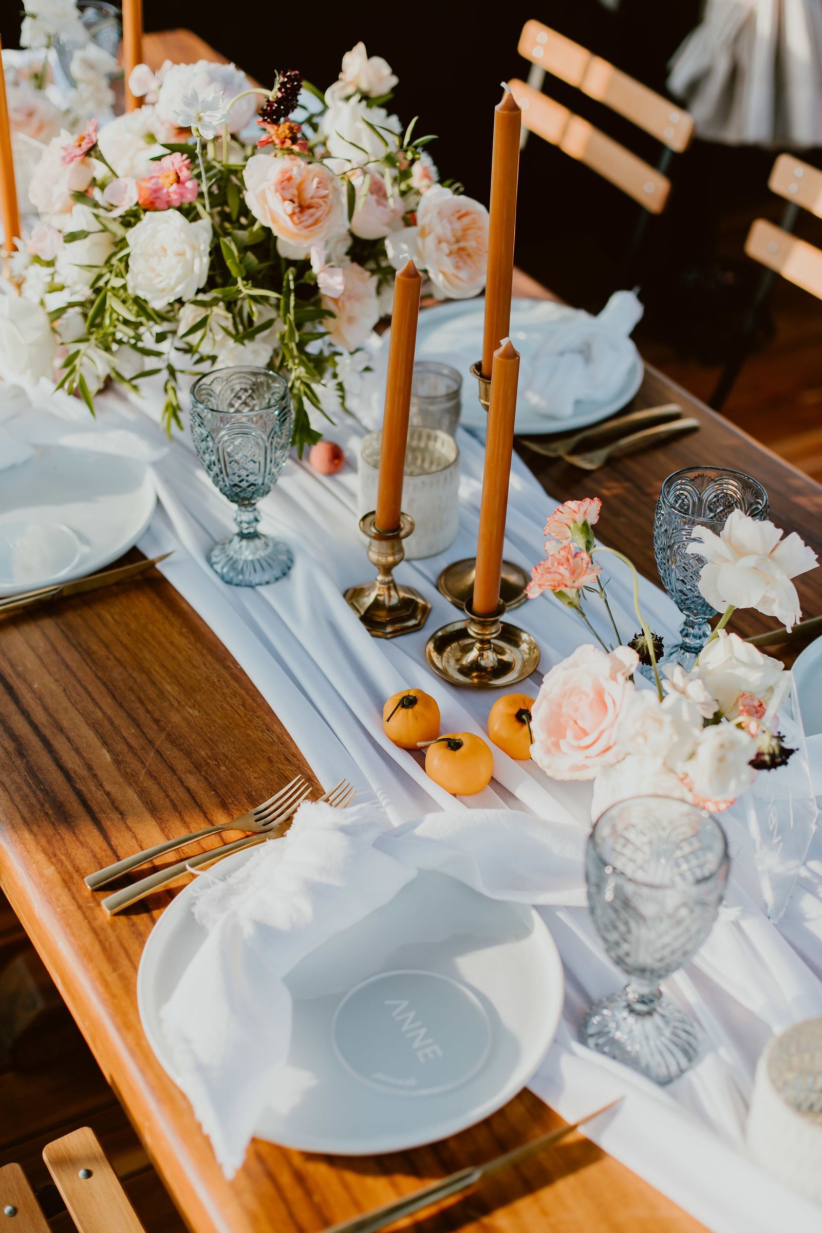 Beautiful table setup with white chargers, white napkins and beautiful table runners. There were brown candle sticks to match the papayas and beautiful wood tables to match. Candles and Flower centerpieces throughout the tables made it look full but still clean.