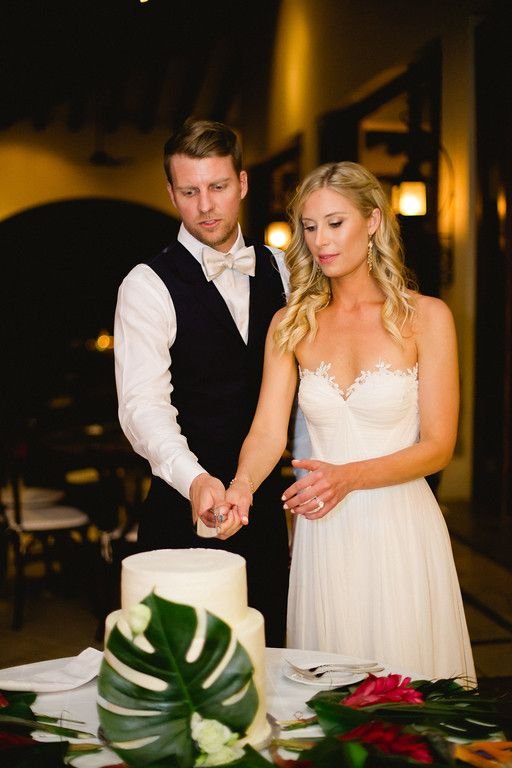 Bride and groom doign their cake cutting with the prettiest and most unique wedding cake. They had one large monstera leaf that looked beautiful. Wedding cake, design and planning by Cabo Wedding Services