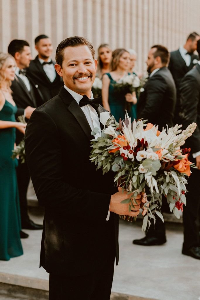 Groom standing at his Wedding Venue, Acre Baja with the Bridal Bouquet. He looked stunning, even with flowers!